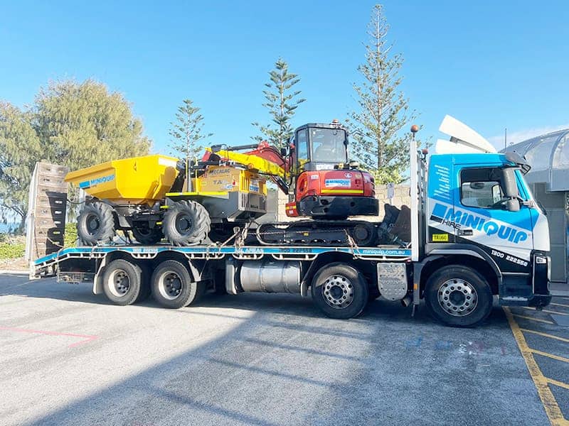 Concrete machinery transport on a flatbed truck for mini equipment hire services.